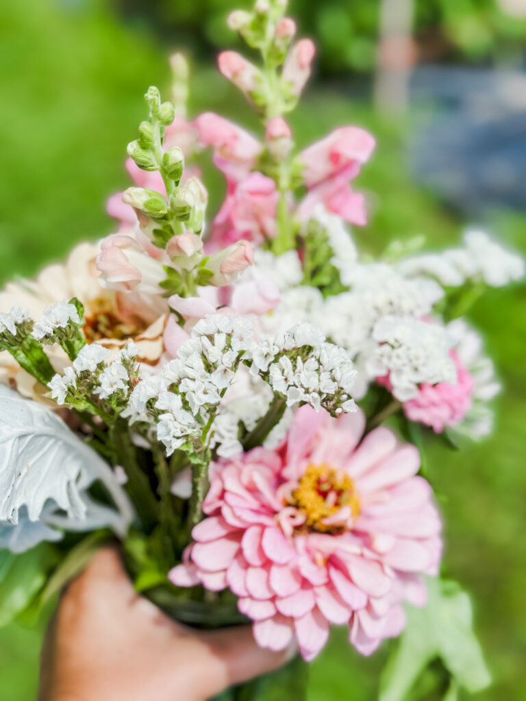 An arrangement of wild flowers being held. Some of the flowers are pink with yellow centers and some are white.