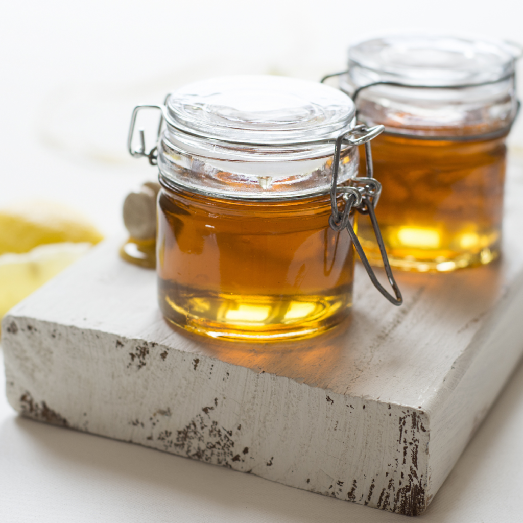 Two Jars of honey on a wooden board. The board is white. The jars have lids with clamps on them.